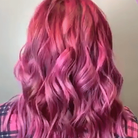 A person with 3 shades of Magenta hair turns and smiles, facing the camera. 