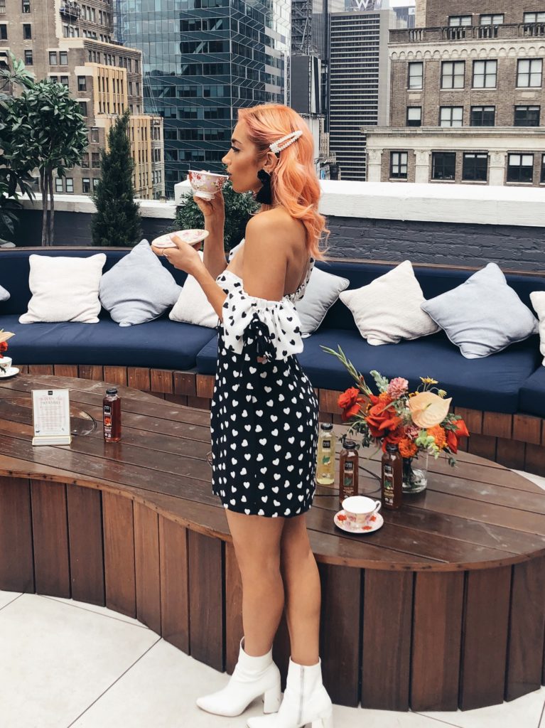 Person with coral hair sips a drink while wearing a polka dot dress