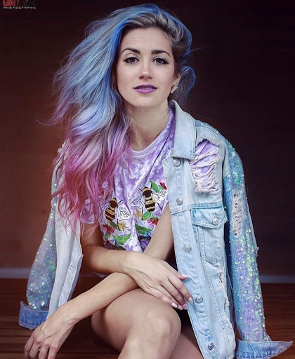 Person with Pastel Blue on top of head and Extreme Pink on the ends wears a jean jacket and looks at the camera