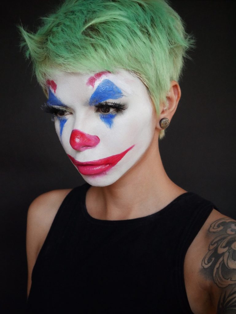 A person in clown like makeup with pastel green Halloween hair 