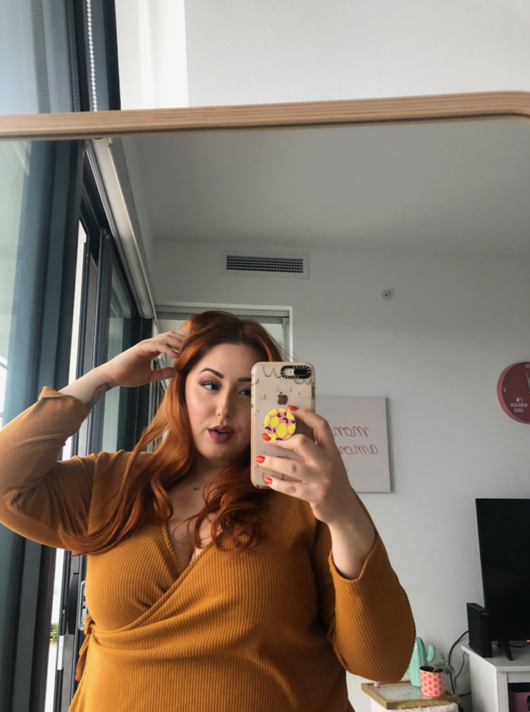Person in an orange shirt with Ginger hair takes a picture in the mirror.